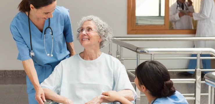 an elder smiles up at a health care professional wearing blue scrubs and a stethoscope